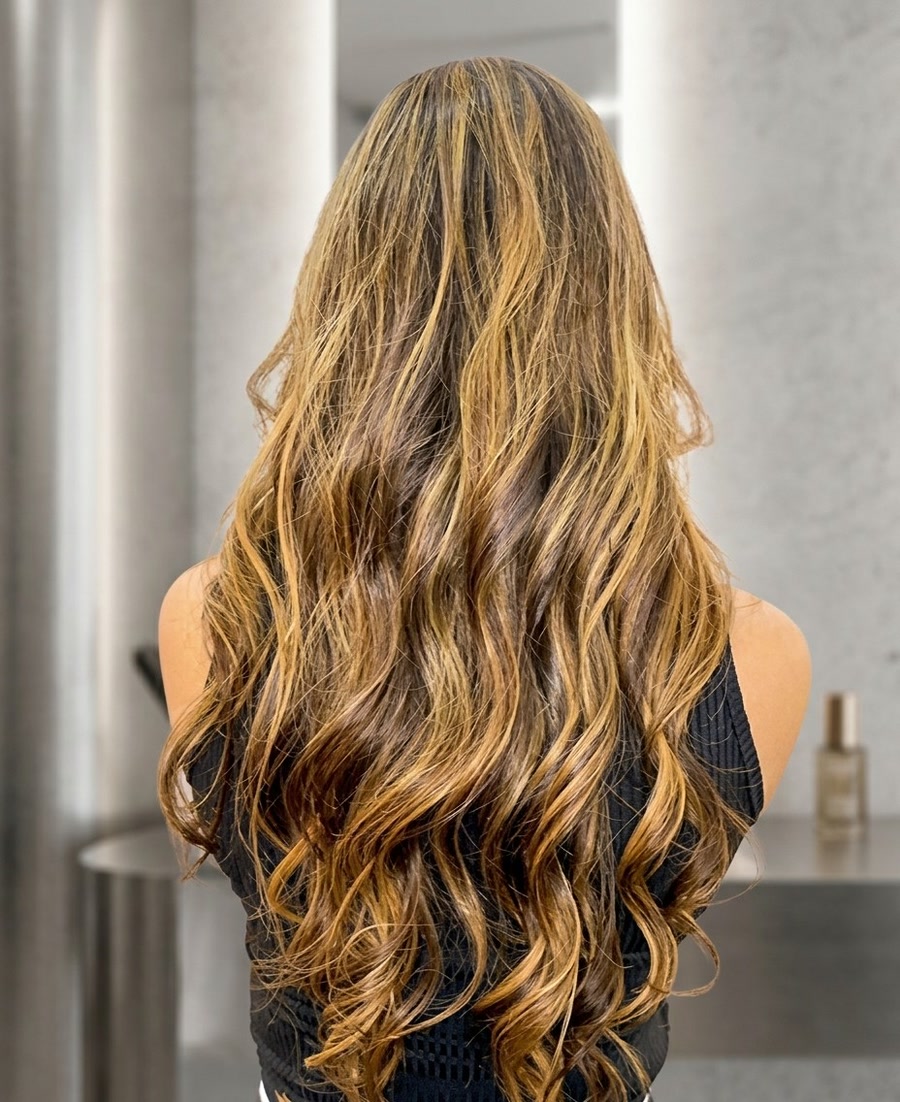 Cabelo longo e ondulado com mechas mel e douradas, visto de costas